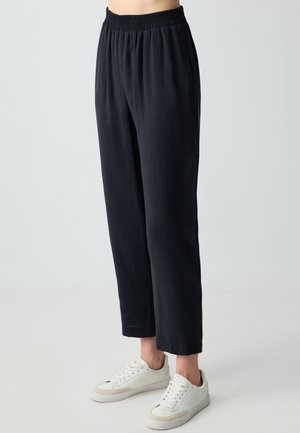 Pantaloni neri, leggeri e dal fit morbido con elastico in vita, accorciati alla caviglia. Indossati con sneaker bianche. Tessuto liscio.