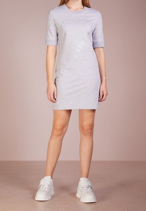 Grijze jurk met korte mouwen, versierd met een hartontwerp en het woord 'LOVE' in zilverkleurige accenten, gemaakt van gladde stof met een losse pasvorm. Gecombineerd met witte sneakers.