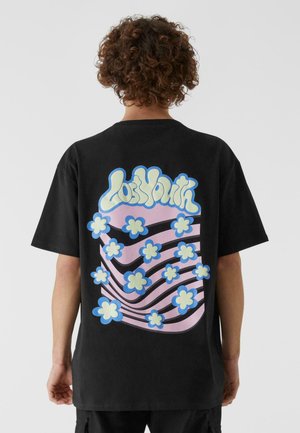Schwarzes Baumwoll-T-Shirt mit einem bunten, blumen- und wellenförmigen Muster in Pastellfarben auf der Rückseite, mit dem Text "Los North" in einer verspielten Schriftart.