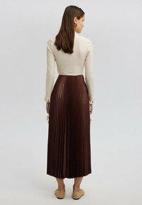 Long pleated brown skirt with a fitted cream top. Top features long sleeves and lace accents at the cuffs. Smooth texture throughout.