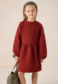 Rood gewatteerde jurk met hartpatroon, lange pofmouwen, ronde halslijn en een taille die is cinched. Vergezeld door een handtas met luipaardprint.