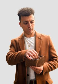 Brown leather wallet held open with cards visible; worn by a man in a brown coat over a white shirt, against a grey background.