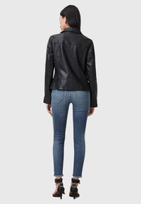 Chaqueta de cuero negra con un diseño ajustado, que presenta un cuello con muesca y puños con cremallera, combinada con vaqueros pitillo azul claro.