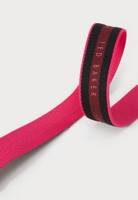 Rózsaszín szövetszalag fekete és bordó csíkkal, rajta a "TED BAKER" felirat. A felület sima és szőtt, élénk színkontrasztot mutat.