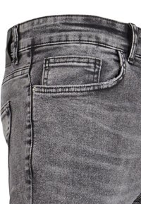 Gros plan sur un jean en denim noir délavé montrant la poche avant droite et les passants de ceinture avec des détails de couture visibles.