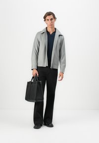 Gray zip-up jacket, navy shirt, black trousers, and black tote bag. The outfit features a minimalist design with clean lines and smooth textures.
