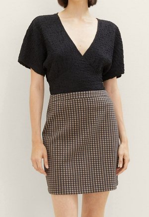 Vrouw draagt een zwarte, gestructureerde korte mouw V-hals top en een hoog taillebruine en zwarte geruite rok.