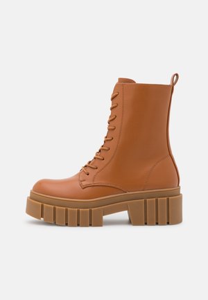 Bottines en cuir marron avec une plateforme et un talon épais, dotées d'un laçage sur le devant et d'un détail boucle à l'arrière.