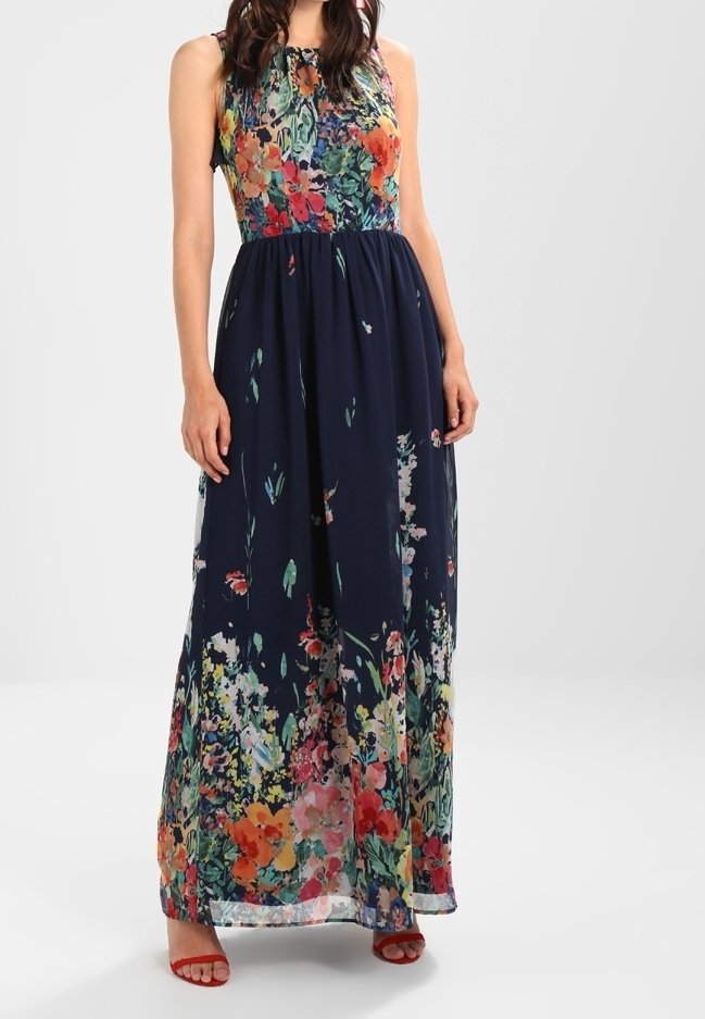 Ärmlös maxiklänning med åtsittande blommig bodice och marinblå kjol med flerfärgade blommönster, bärs med röda öppna klackskor.