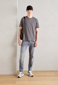 T-shirt en coton gris à manches courtes, associé à un jean bleu clair. Casquette noire et baskets blanches avec des accents argentés. Sac à épaule marron simple.