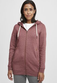 Bordeaux zip-up hettegenser med fleece-struktur, snorhette, to sidelommer med trekantede brune detaljer og ribbestrikkede mansjetter.
