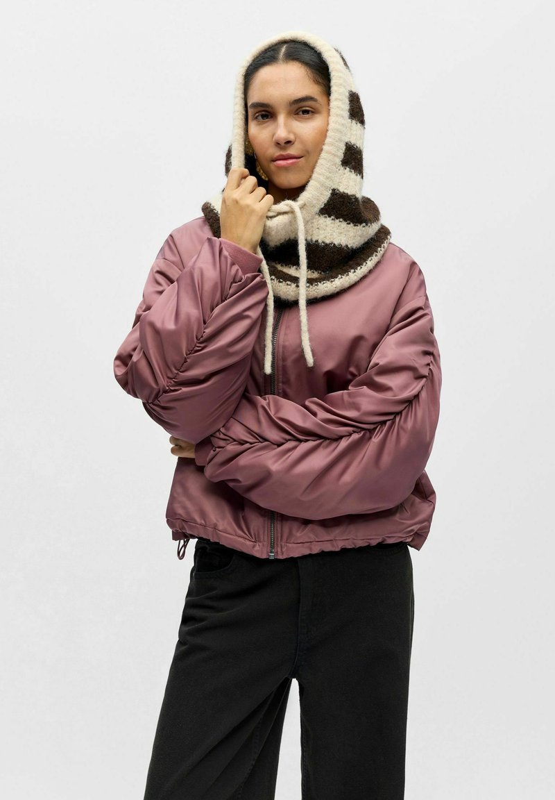 Veste aviateur matelassée et raccourcie en satin mauve avec des manches volumineuses, associée à une écharpe à capuche rayée crème et marron en maille.