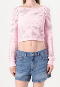 Różowy sweter w crop top z długimi rękawami i wzorem motyla, połączony z szortami dżinsowymi o wysokim stanie. Materiał wydaje się lekki.
