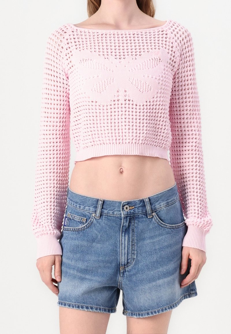 Różowy sweter w crop top z długimi rękawami i wzorem motyla, połączony z szortami dżinsowymi o wysokim stanie. Materiał wydaje się lekki.