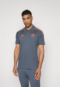 Grå polo shirt med lyserøde striber og logo på brystet. Fremstillet af åndbart materiale, med klassisk krave og korte ærmer.