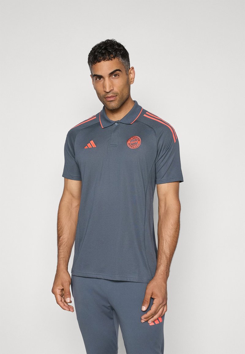 Grå polo shirt med lyserøde striber og logo på brystet. Fremstillet af åndbart materiale, med klassisk krave og korte ærmer.