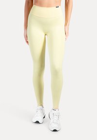 Ljusgula leggings med hög midja, gjorda av stretchigt tyg. Kombinerade med vita träningsskor med svarta detaljer.