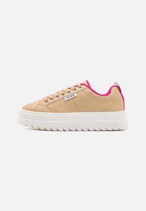 Beżowy niski sneaker z grubą białą podeszwą, różowym wnętrzem, beżowymi sznurówkami i małą białą metką "HUGO" po boku.