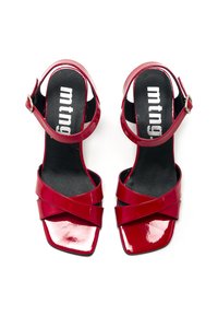 Tacones altos de charol rojo con tiras cruzadas, punteras cuadradas y detalle de hebilla en el tobillo. La planta negra presenta el logo de la marca.