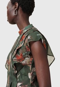 Green floral blouse featuring a ruffled design, with a high collar and flowing sleeves. Made of lightweight fabric with vibrant print details.