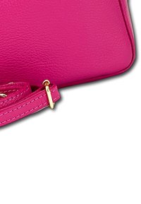 Heldere roze leren handtas hoek met bijpassende verstelbare schouderband en gouden metalen gesp op een witte achtergrond.