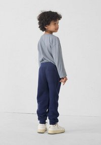 Grijze lange mouwen shirt en marineblauwe joggers gemaakt van zachte stof. Joggers hebben zijzakken; model draagt beige sneakers.