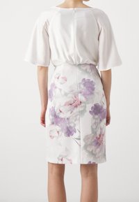 Robe fleurie avec un haut en satin crème à manches larges, se transformant en une jupe crayon avec un imprimé floral violet et rose. Fermeture éclair à l'arrière.