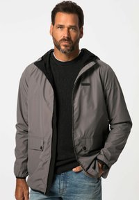 Lettet, grå jakke med sort hætte og lynlåslukning, der har to sidelommer og elastiske manchetter. Båret over en struktureret sort sweater.