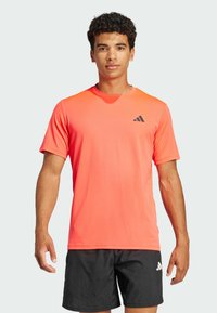 Camiseta atlética de color naranja brillante con mangas cortas, cuello redondo y un acento de logo negro en el pecho; textura suave, tejido ligero.
