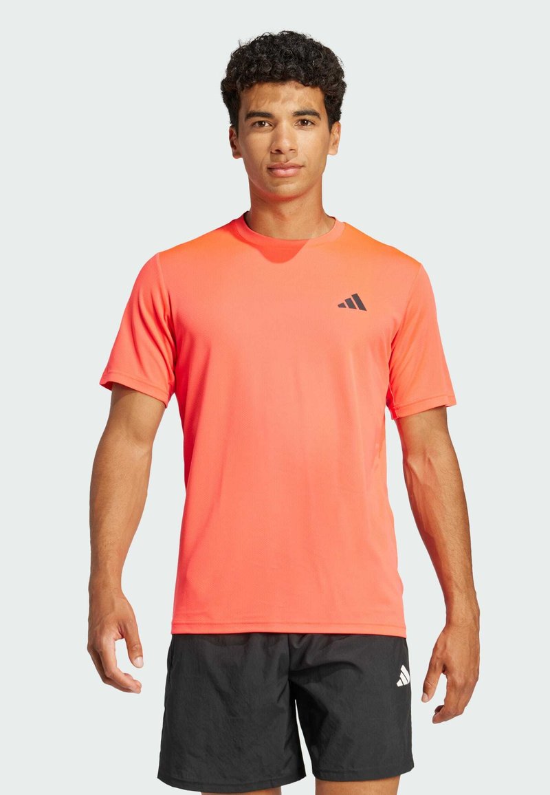 Camiseta atlética de color naranja brillante con mangas cortas, cuello redondo y un acento de logo negro en el pecho; textura suave, tejido ligero.