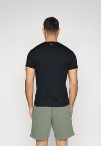 Zwart katoenen t-shirt met korte mouwen en een ronde hals, weergegeven vanuit de achterkant. Vergezeld door olijfgroene shorts.