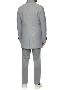 Grijze wollen jas in een mix met een gestructureerde kraag, een getailleerde pasvorm en een rugventilatie, gecombineerd met grijze relaxed-fit broek en witte sneakers.