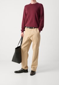 Rotes Langarmhemd, beige Hose, schwarzer Gürtel, schwarze Ledertasche und schwarze Stiefel. Einfaches, lässiges Outfit mit minimalistischen Details.