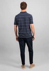 Polo s krátkým rukávem v námořnické modři s bílými a světle modrými pruhy, v kombinaci s tmavými zúženými kalhotami a béžovými slip-on botami. Hladký materiál.
