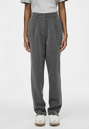 Pantalons gris sur mesure avec une taille plate, passants de ceinture et une fermeture à un seul bouton, fabriqués dans un tissu texturé, associés à des baskets blanches.
