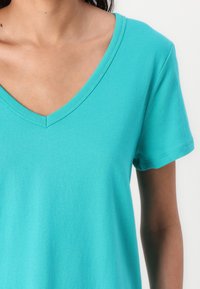 Turkis V-hals t-shirt lavet af blødt bomuldsstof, med korte ærmer og en glat tekstur, der har et enkelt og rent design.