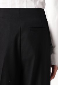 Pantalons noirs ajustés avec une texture lisse, dotés d'une poche arrière unique, de détails de couture subtils et d'une coupe classique.