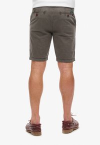 Pantalones cortos de chino gris para hombre con un corte ajustado, con bolsillos traseros y detalles de costura sutiles, combinados con zapatos de barco color burdeos.