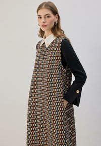 Tekstūruota berankovė suknelė su geometriniu raštu juodos, raudonos, geltonos ir baltos spalvų. Suknelėje kontrastingas baltas apykaklės ir juodos rankovės.