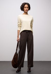 Crèmekleurige trui met lange mouwen, gecombineerd met loszittende, donkerbruine broek. Outfit compleet met een bruine schoudertas en donkere enkellaarsjes.