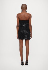 Rochie mini neagră fără bretele, cu un model texturat, având o siluetă ajustată și accente lucioase. Purtați cu tocuri negre.