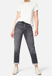 Jeans de mezclilla gris con un corte relajado, cierre de cinco botones y puños enrollados, combinados con una camiseta blanca sencilla y zapatillas ligeras.