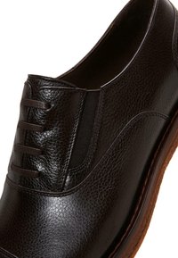 Schwarzer Lederschuh mit strukturiertem Oberflächen, elastischen seitlichen Einsätzen und einer genähten Detail entlang der oberen Kante. Flache Gummisohle.