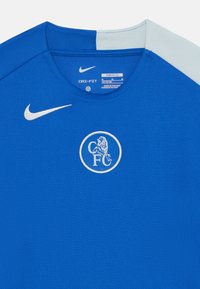 Blå Dri-FIT trøye med rund hals, med et hvitt løve-symbol og en hvit Nike-logo på venstre skulder. Teksturfabrikk, slim fit.