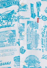 Camicetta a maniche corte in cotone bianco con stampa blu di etichette e loghi vintage Levi's, con chiusura a bottoni classica.