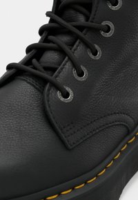 Black leather boot with round toe, textured surface, black laces, silver eyelets, and yellow stitching along the sole edge.