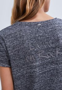 Gray t-shirt with a textured finish, featuring the phrase "La vie en Rock" in a light, script font on the back. Short sleeves.
