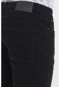 Mustad teksapüksid tekstuurse viimistlusega, millel on pealõikega tagatasku ja nahast vöökohatükk. Sisaldab kulunud külgedetaili.