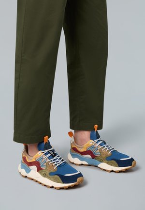 Mehrfarbige Sneakers mit blauen, braunen, grünen und gelben Wildleder- und Mesh-Obermaterial, weißen Schnürsenkeln und Gummisohlen, kombiniert mit olivgrünen Hosen.
