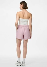 Shorts roses clairs avec une taille élastique et des poches latérales. Tissu doux avec une coupe ample, associés à un top tube blanc et des chaussures de sport.